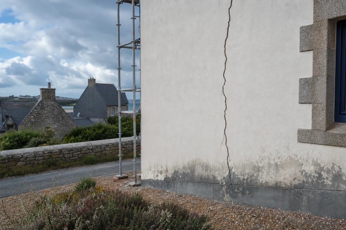 Fissure verticale sur un mur enduit, avec traces d&rsquo;humidité en pied de façade